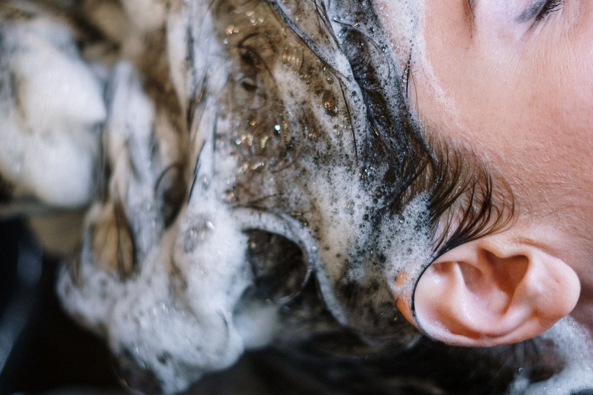 A client having shampoo foam massaged through her hair at a salon sink