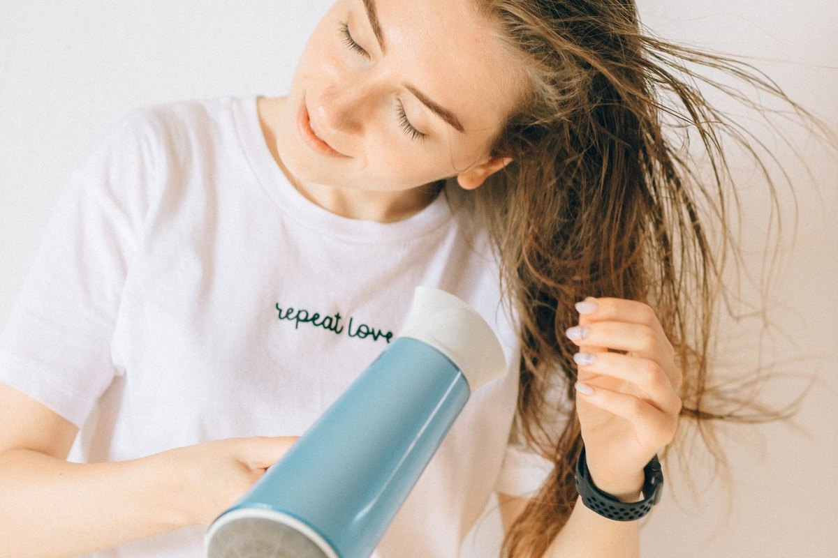 A woman drying her long hair at home with a compact blow dryer