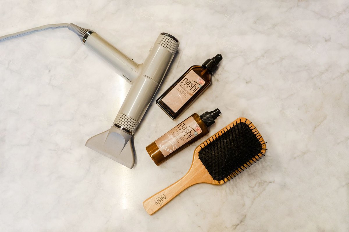 Flat lay of a hair dryer, brush and styling bottles