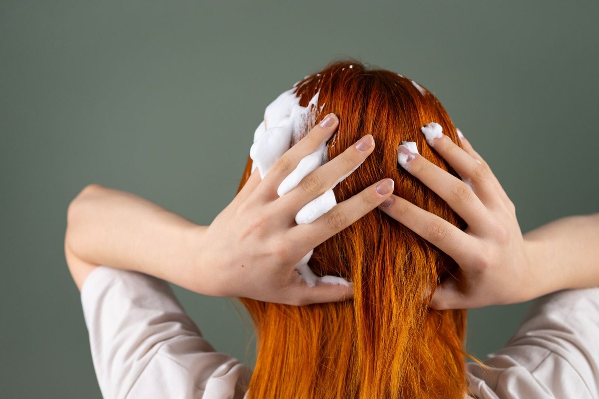 Back view of a woman washing shampoo through long hair