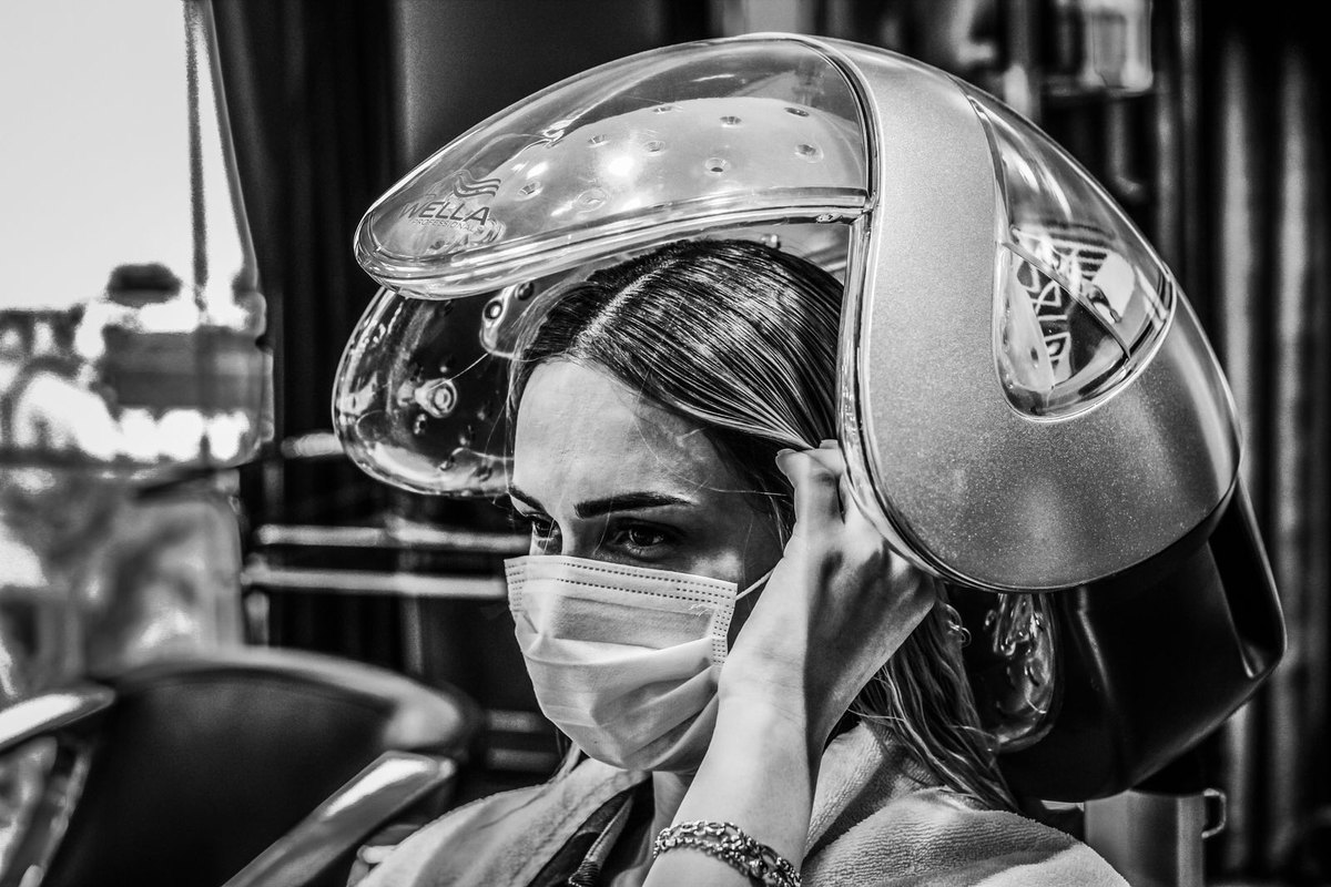 A client under a salon hair steamer, in black and white