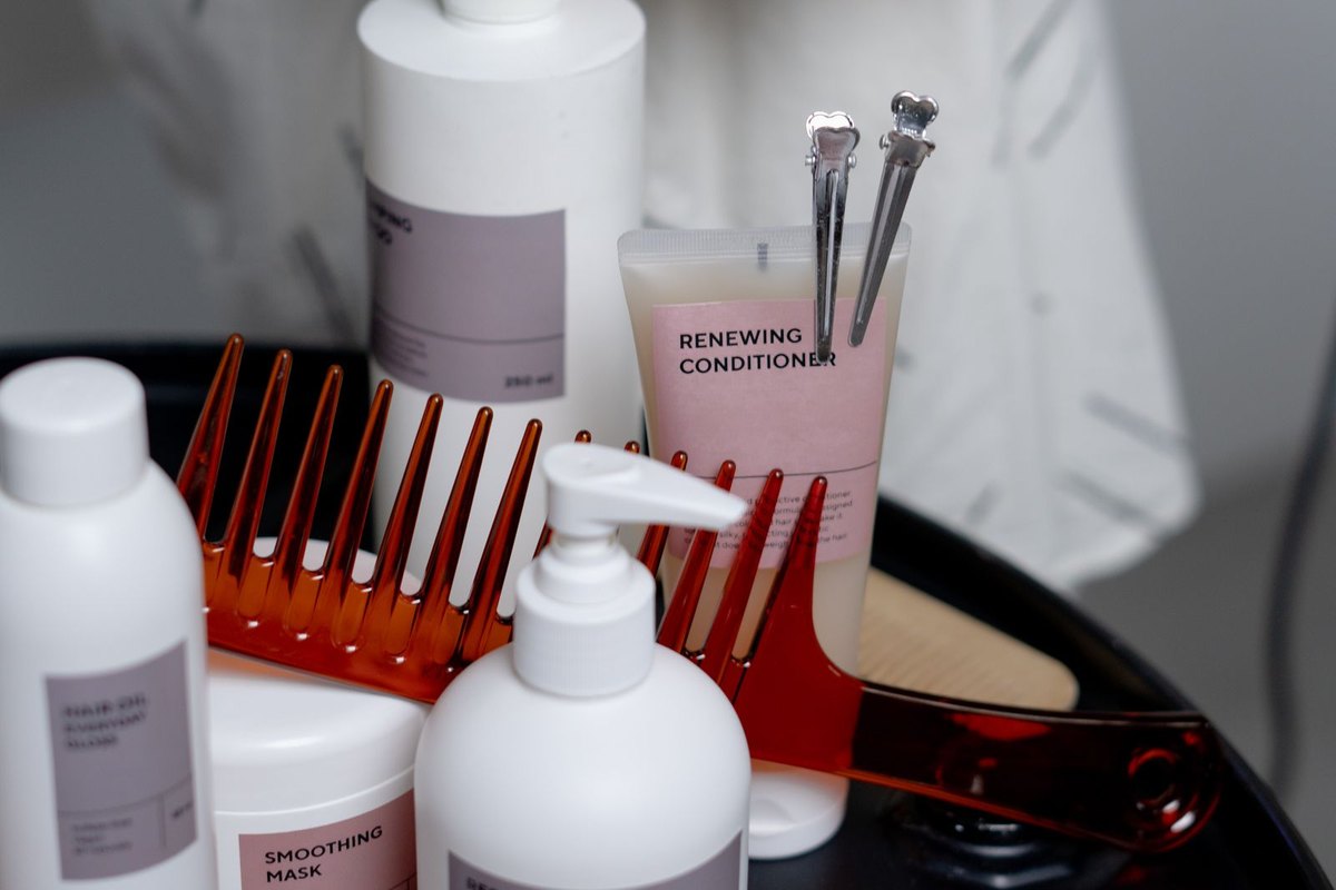 Salon tray with unbranded white shampoo, conditioner and hair mask bottles beside a comb