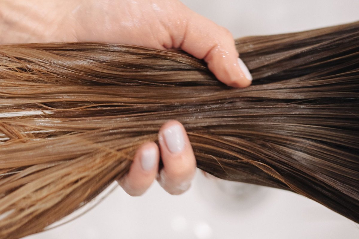 A hand holding a wet section of hair over a salon basin
